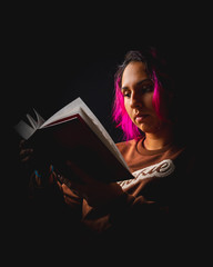 Portrait of young woman reading a book on black background low key