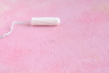 White hygiene tampon with selective focus for monthly women’s menstrual days. Clean cotton absorbent tampon on pink abstract textured background. Protect care pad for female menstruation period day 