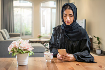 Beautiful muslim woman wearing abaya using smart phone while sitting at her luxury apartment.