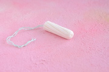 White hygiene tampon with selective focus for monthly women’s menstrual days. Clean cotton absorbent tampon on pink abstract textured background. Protect care pad for female menstruation period day 