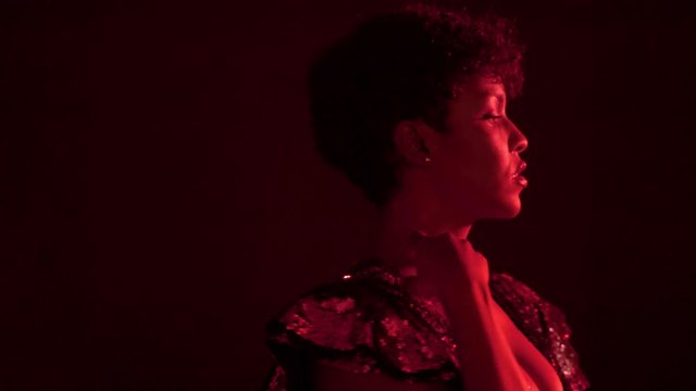 mixed race black woman dancing and smiling in night club in red light. Wears sparkly sequin dress