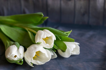 A bouquet of white tulips is on the table , the background is wooden.
