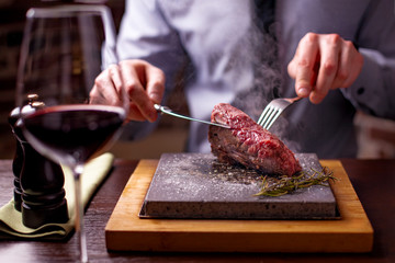 sirloin steak on a very hot stone being cooked by a man to his own taste on a wooden table with a knife and fork