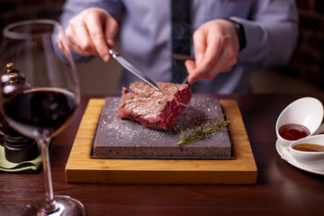 sirloin steak on a very hot stone being cooked by a man to his own taste on a wooden table with a...