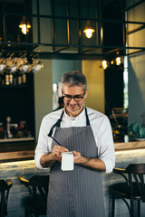 senior barman standing in front of counter and taking orders in restaurant