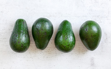 Four whole avocado pears on white board shot from above.
