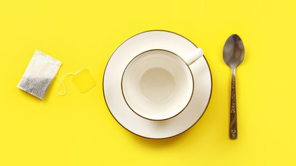 Flat lay photo, tea bag, empty porcelain cup and spoon on yellow board.