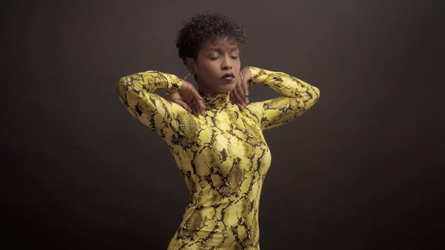 mixed race african american woman in bright yellow dress with python print. 90's style, lift up her hands