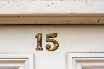 House number fifteen with the 15 in bronze broad numbers on a white wooden door frame