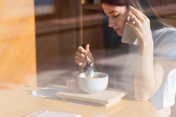Stylish woman picks up a breakfast in a morning cafe on a smartphone for an instagram. Tasty morning breakfast - granola