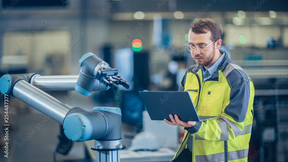 Aufkleber At the Factory: Automation Engineer Uses Laptop for Programming Robotic Arm. New Era in Automatic Manufacturing Industry.