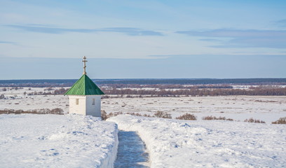 Winter landscape with small white chapel on  bank of  snow-covered river