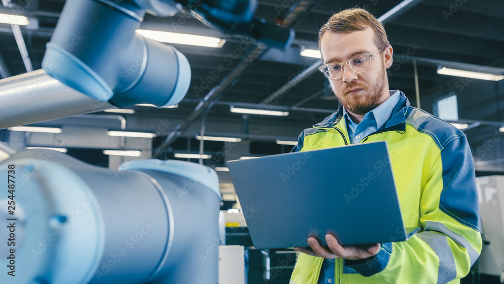 Aufkleber At the Factory: Automation Engineer Uses Laptop for Programming Robotic Arm. New Era in Automatic Manufacturing Industry.