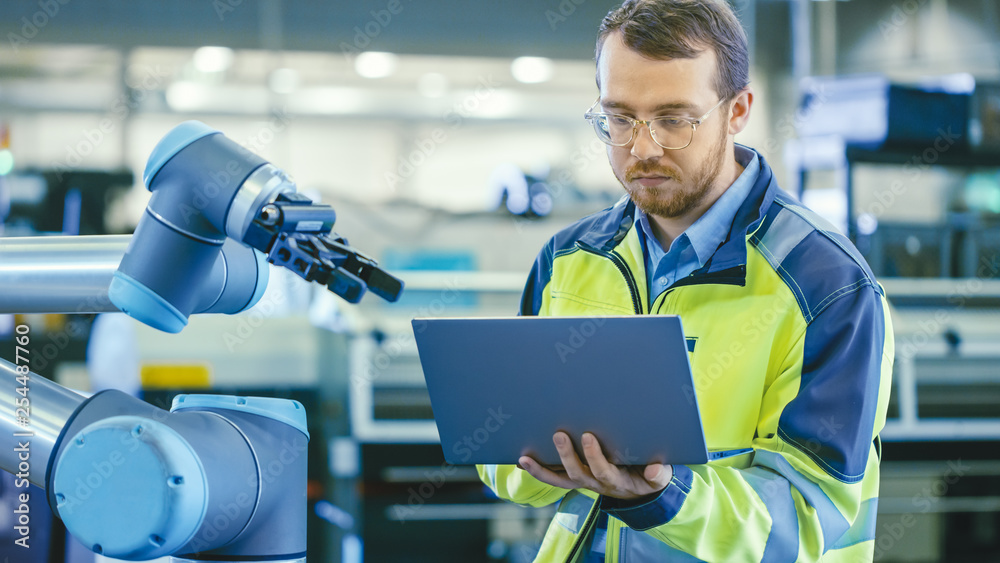 Poster At the Factory: Automation Engineer Uses Laptop for Programming Robotic Arm. New Era in Automatic Manufacturing Industry.