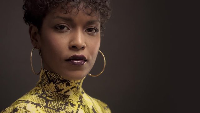 mixed race african american woman in bright yellow dress with python print. 90's style Turning face to the camera and smiling, touches her earrings