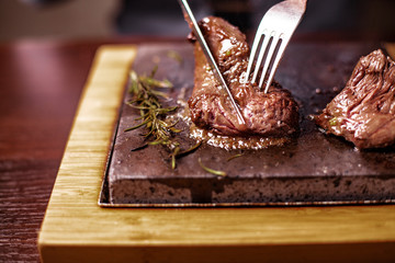 sirloin steak on a very hot stone being cooked by a man to his own taste on a wooden table with a knife and fork