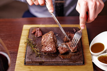 sirloin steak on a very hot stone being cooked by a man to his own taste on a wooden table with a knife and fork