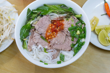 Soup pho in a budget restaurant in Danang city, Vietnam for 35 000 dongs. Noodles, sliced boiled beef, basil leaves, chopped spring onion. Sprouts, chili and pieces of lime on the plate.