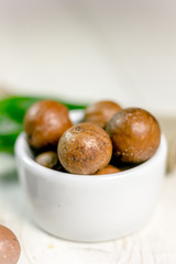 White ceramic bowl with macadamia nuts over the wooden table.