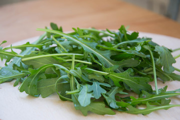 Green arugula leaves on wooden cutting board. Fresh rucola in the kitchen in plastic tray, Italian seasoning. Healthy lifestyle organic food