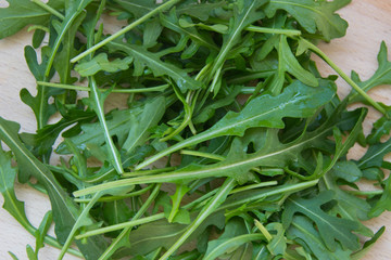 Fototapeta premium Green arugula leaves on wooden cutting board. Fresh rucola in the kitchen in plastic tray, Italian seasoning. Healthy lifestyle organic food