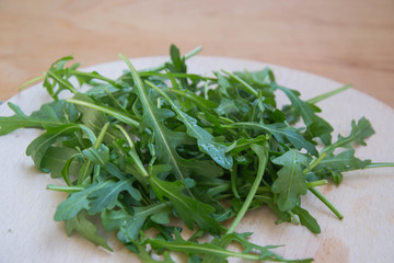 Green arugula leaves on wooden cutting board. Fresh rucola in the kitchen in plastic tray, Italian seasoning. Healthy lifestyle organic food