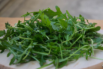 Green arugula leaves on wooden cutting board. Fresh rucola in the kitchen in plastic tray, Italian seasoning. Healthy lifestyle organic food