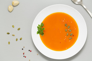 Pumpkin soup with herbs, cream and pumpkin seeds served in white bowl. Seasonal autumn food - Spicy pumpkin soup. Top view. 