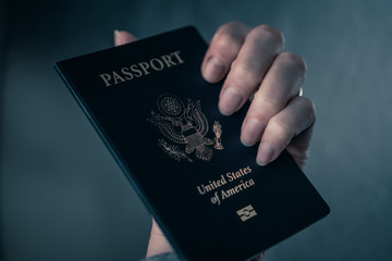 Female hand holding Passport of USA on blurred silver background.