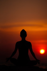 Fototapeta premium Yoga near the sea at sunset. Meditation and relaxation. Siluet.