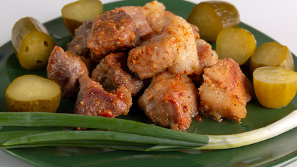 Hot pork slices. Delicious baked crispy slices of pork have a beautiful color, and pickles and green onions lie in a green dish. Appetizing and delicious freshly prepared meat dishes.