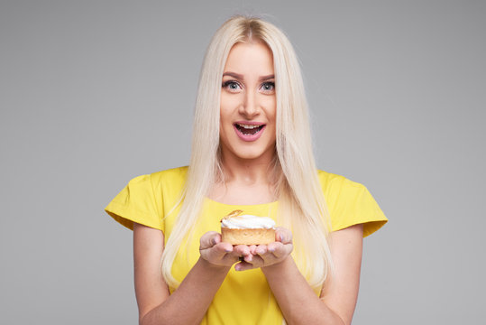Diet concept. Healthy Food. Young smiling blond Woman in yellow dress With pleasure tasting dessert isolated on grey background. Birthday cupcake  - Powered by Adobe