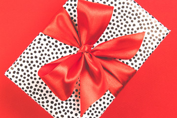 Gift box with red satin bow on a red background. Festive concept. Top view.