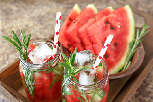  Two jars of refreshing summer drink with watermelon and rosemary served on a wooden tray. Watermelon and rosemary infused water with ice. Concept of healthy diet, cleansing the body, losing weight.