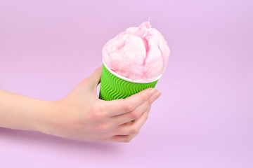 Bright pink candy cotton in plastick cup in woman hand on lilac background.