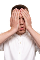 Fototapeta premium Charming handsome young man in a white shirt is making faces, while standing isolated on a white background