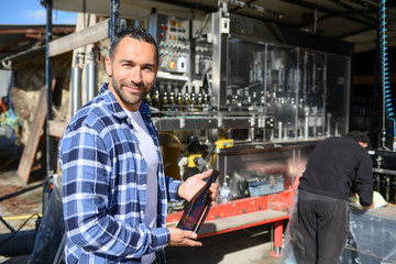 young man wine maker working filling wine bottle with automatic bottling machine