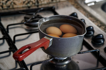 Boiled eggs in dipper of water on the kitchen stove