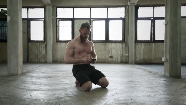 Shirtless man using phone while kneeling
