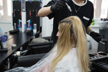 Professional hairdresser putting color mask dyeing hair of woman in beauty salon
