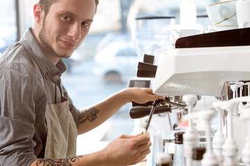 Cleaning carefully. Closeup portrait of a handsome smiling barista wiping and cleaning coffee machine