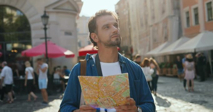 Close up of the attractive Caucasian young man holding and reading a map while being a tourist in a new town.
