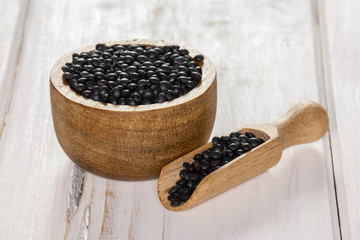 Lot of whole black lentils beluga variety scoop with wooden bowl on white wood