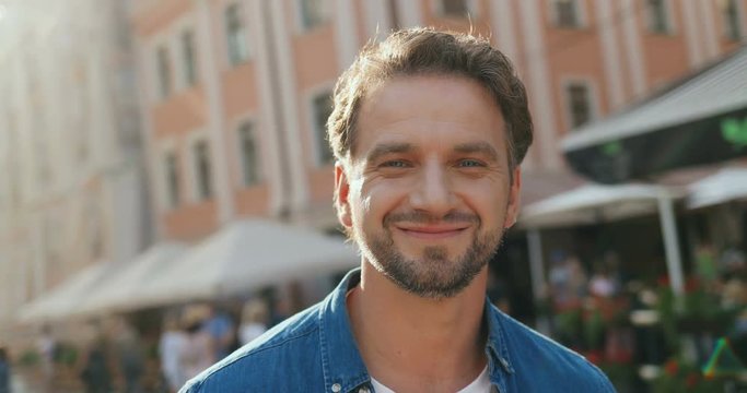 Portrait of the attractive young man looking at the side, then turning head to the camera and smiling cheerfully. Close up.