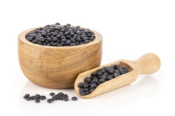 Lot of whole black lentils beluga variety with wooden bowl isolated on white background