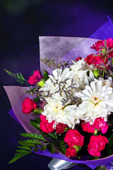 Bouquet of white and red flowers in purple paper on black background, vertical photo