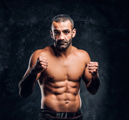 Obraz premium Professional Muay Thai boxer with naked torso posing for a camera. Studio photo against a dark textured wall