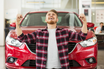 Happy handsome man buying a new car at the dealership