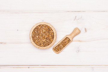 Lot of whole raw bulgur grains in a scoop with wooden bowl flatlay on white wood