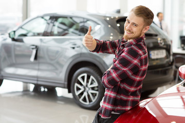 Happy handsome man buying a new car at the dealership